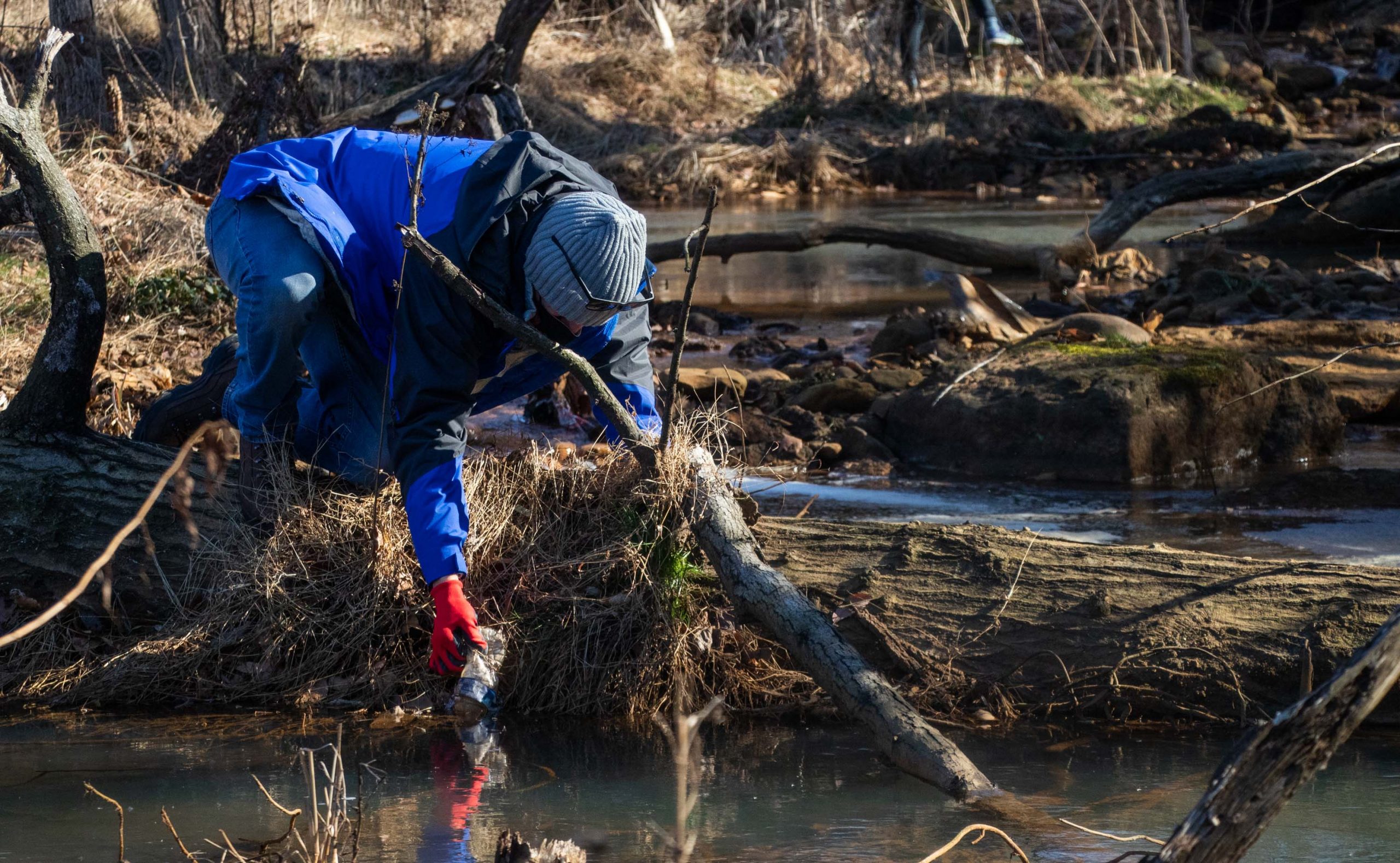David Bloodgood pulls out a water bottle from the stream Saturday during the cleanup at Pope Branch Park.  (Isabel Miller | Medill News Service)